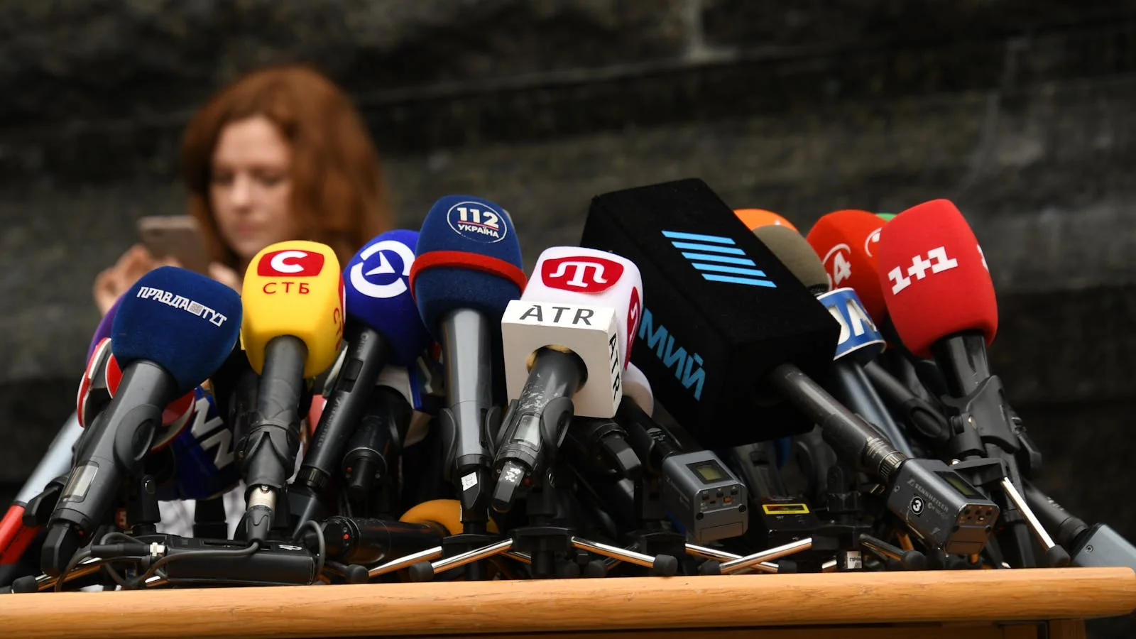 Microphones clustered at a press briefing podium, the surface where a kept follow-up update either restores trust or doesn't